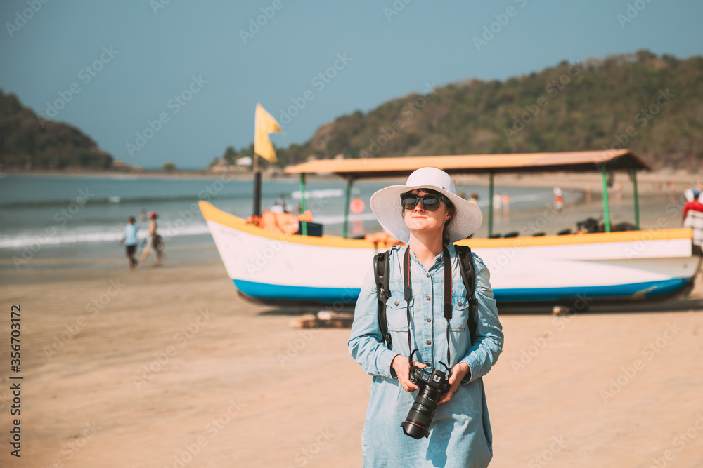 Fototapeta premium Canacona, Goa, India. Young Caucasian Lady Woman With Camera Standing On Famous Palolem Beach Near Arabian Sea In Summer Sunny Day