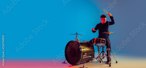Bilde på lerret Caucasian male drummer improvising isolated on blue studio background in neon light