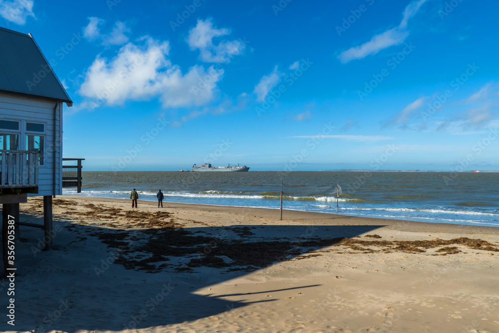 Beach scene with men watching a large ship entering Westerschelde, Netherlands
