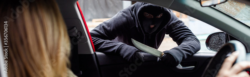 Fotografia Panoramic shot of robber in balaclava holding knife near woman in car