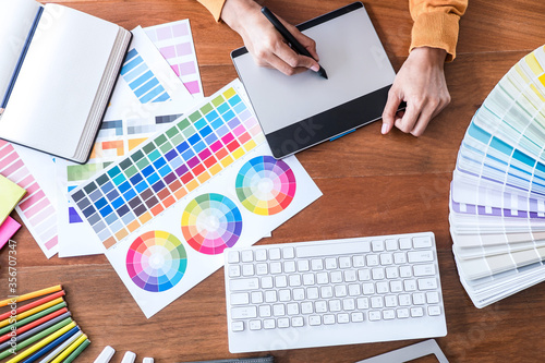 Image of female creative graphic designer working on color selection and drawing on graphics tablet at workplace with work tools and accessories