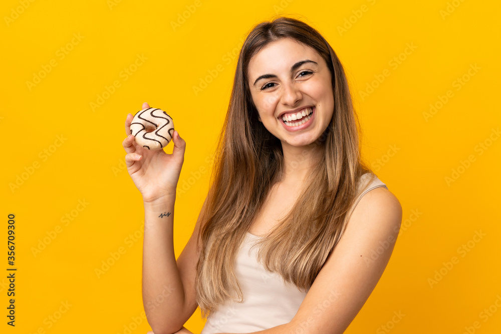Young woman over isolated yellow background holding a donut and happy Young woman over isolated yellow background holding a donut and happy