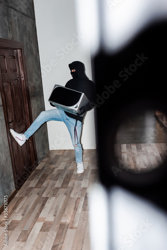 Selective focus of robber in balaclava and leather gloves holding microwave and closing house door © LIGHTFIELD STUDIOS