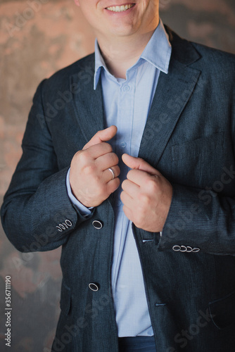 Confident businessman man in the studio straightens a gray jacket with a ring on his hand