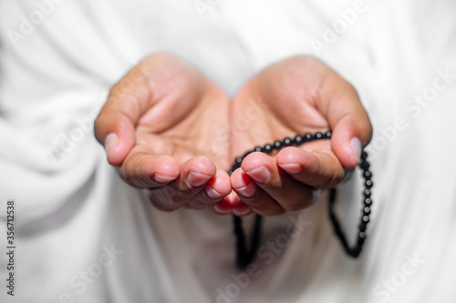 Muslim women raise their hands to pray with a Tasbeeh on white background, indoors. Focus on hands.