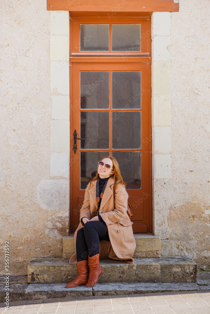 girl in coat sitting on brown background of door of house in retro style.