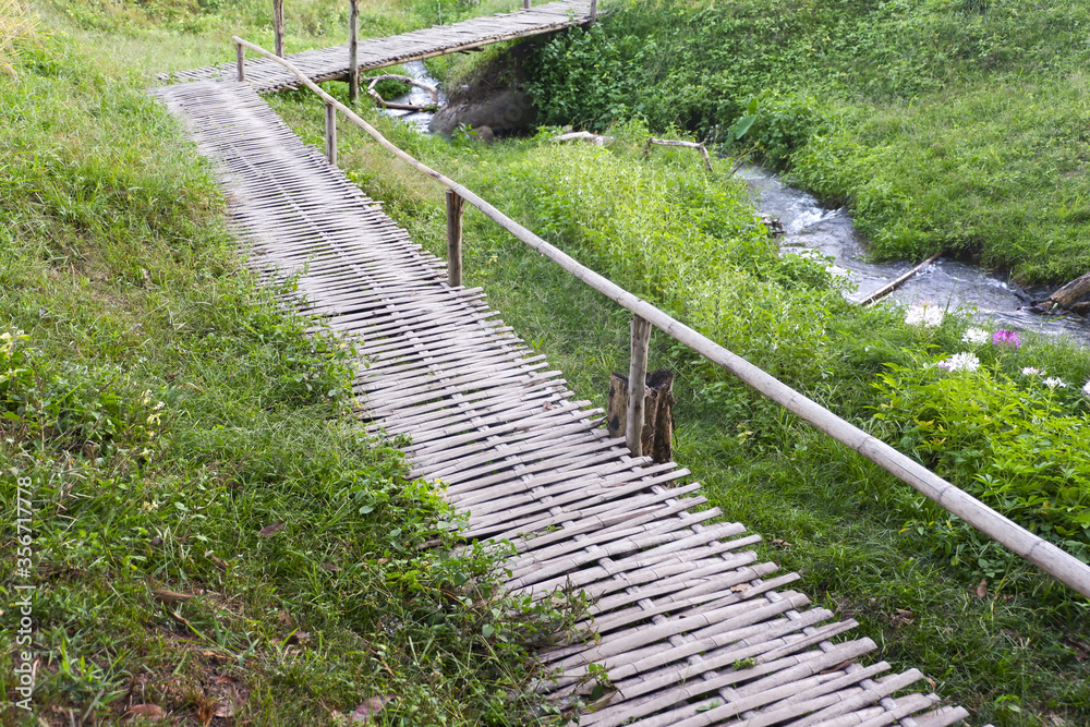 Rural Green grass fields and bamboo bridge,the wooden bridge located in Chiangmai province The Northern of Thailand.Streams parallel to the bridge Rural Green grass fields and bamboo bridge,the wooden bridge located in Chiangmai province The Northern of Thailand.Streams parallel to the bridge