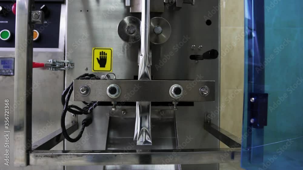 Work process at the enterprise, metal, technically equipped device which packs by means of the heated Press small, silver-colored sticks and fills in them various foodstuff, close-up Work process at the enterprise, metal, technically equipped device which packs by means of the heated Press small, silver-colored sticks and fills in them various foodstuff, close-up