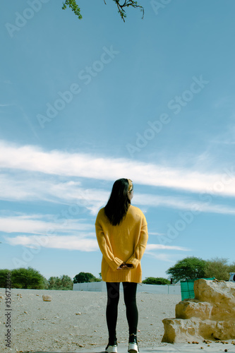 Image of a young woman wears a yellow sweater standing and looking at the horizon.
