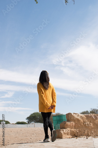 Image of a young woman wearing a yellow sweater looking at the horizon.