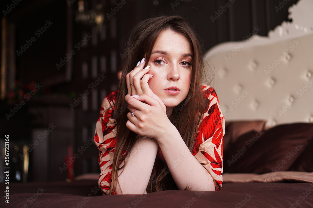 Relaxed woman lying on a brown bed thinking deeply. Woman in retro style room in red dress Relaxed woman lying on a brown bed thinking deeply. Woman in retro style room in red dress