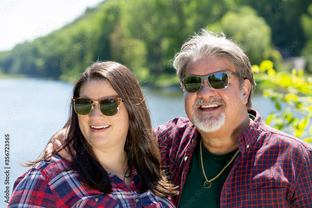 Father and daughter share a day outdoors in the park. They are smiling while posing together. Father and daughter share a day outdoors in the park. They are smiling while posing together.