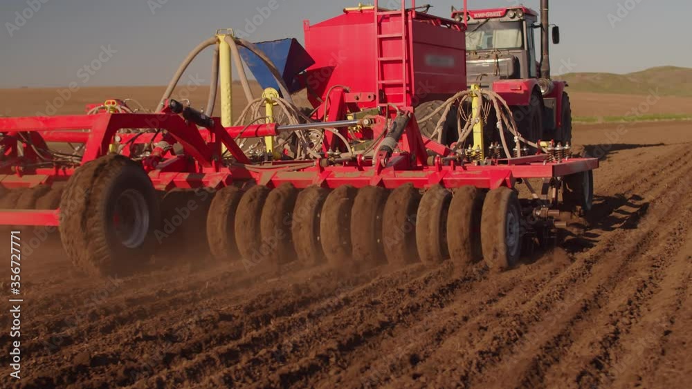 Red seed harvester sows wheat seeds in the field. The machine for sowing seeds works in the field. The seeding machine passes by the operator
