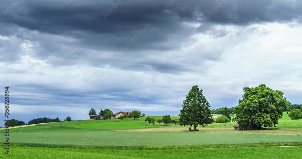 Timelapse de nuages noirs menaçants au-dessus d'un champ de culture avec une ferme et des plantations en suisse romande
