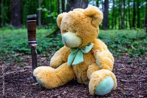 Teddy bear in the woods with a knife. Symbol of loneliness and aggression. For the moderator: an old bear without a brand © vlady1984