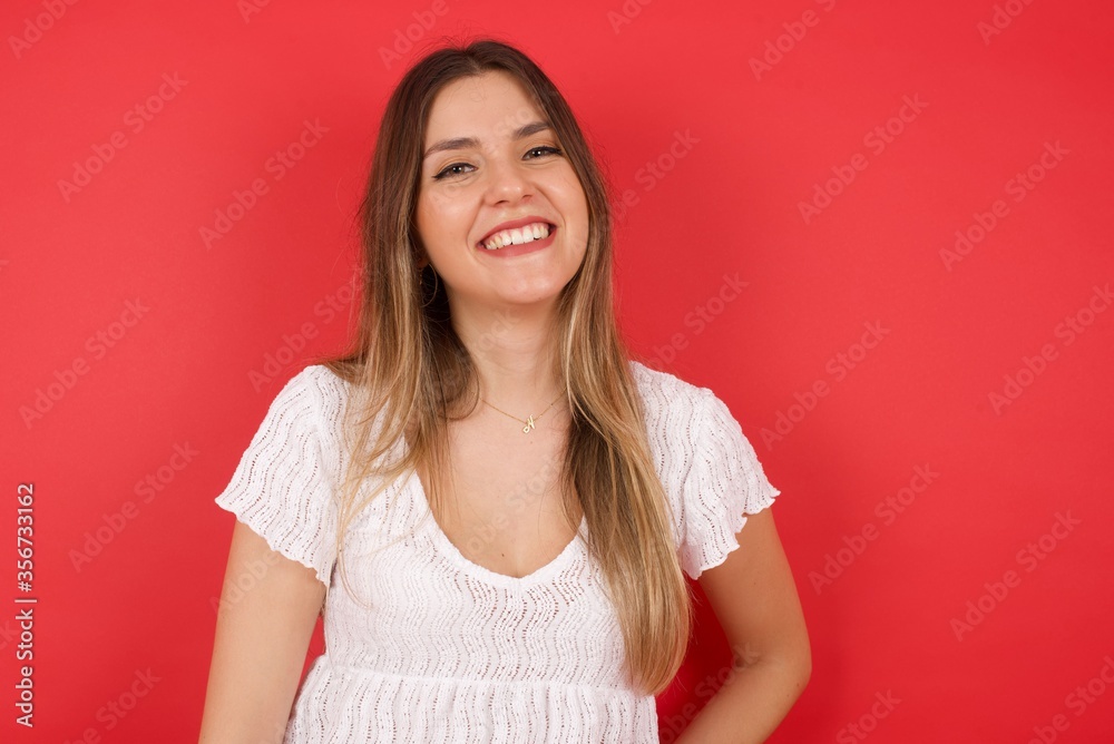 Beautiful smiling brunette female with broad smile, shows white teeth, wears casual t shirt, stands over gray studio wall rejoices having day off. Woman standing indoors. Beautiful smiling brunette female with broad smile, shows white teeth, wears casual t shirt, stands over gray studio wall rejoices having day off. Woman standing indoors.
