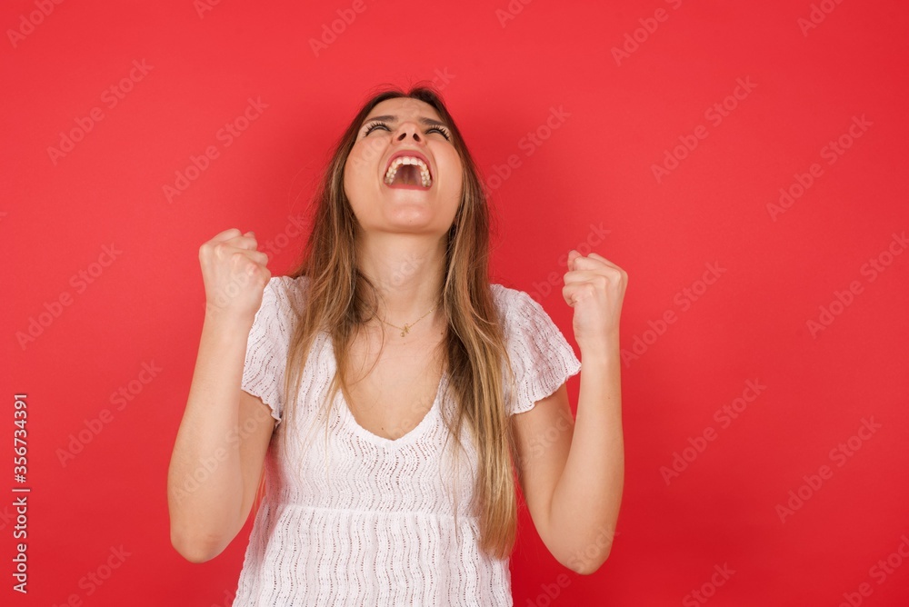 Portrait of beautiful blonde female looks with excitement up, keeps hands raised, notices something unexpected, poses indoors. Lovely woman reacts on sudden news. Portrait of beautiful blonde female looks with excitement up, keeps hands raised, notices something unexpected, poses indoors. Lovely woman reacts on sudden news.