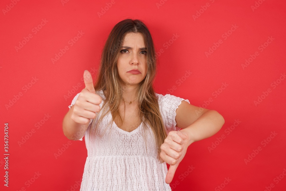 Pretty young pensive woman making good-bad sign. Displeased and unimpressed wearing casual clothes. Pretty young pensive woman making good-bad sign. Displeased and unimpressed wearing casual clothes.