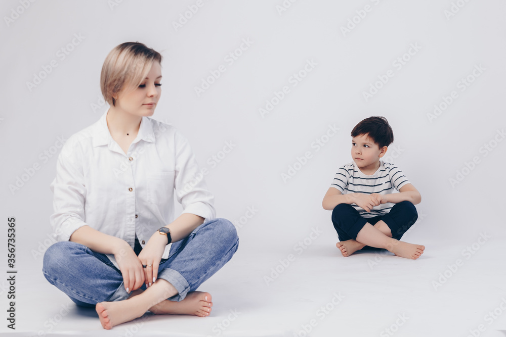 Obraz premium White background. Mom sits in the lotus position in front, her son sits behind as well.