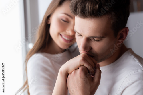 selective focus of man kissing hand of cheerful woman at home