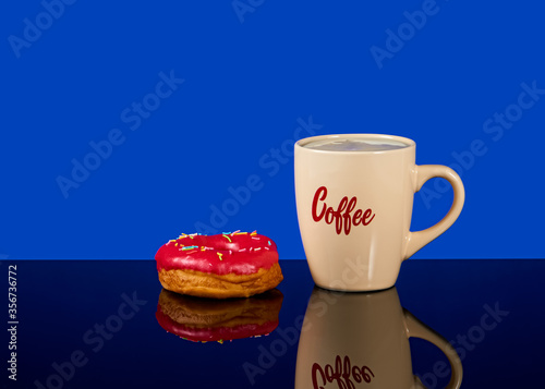 Tasty donut and white cup of coffee with coffee on a blue background with reflection