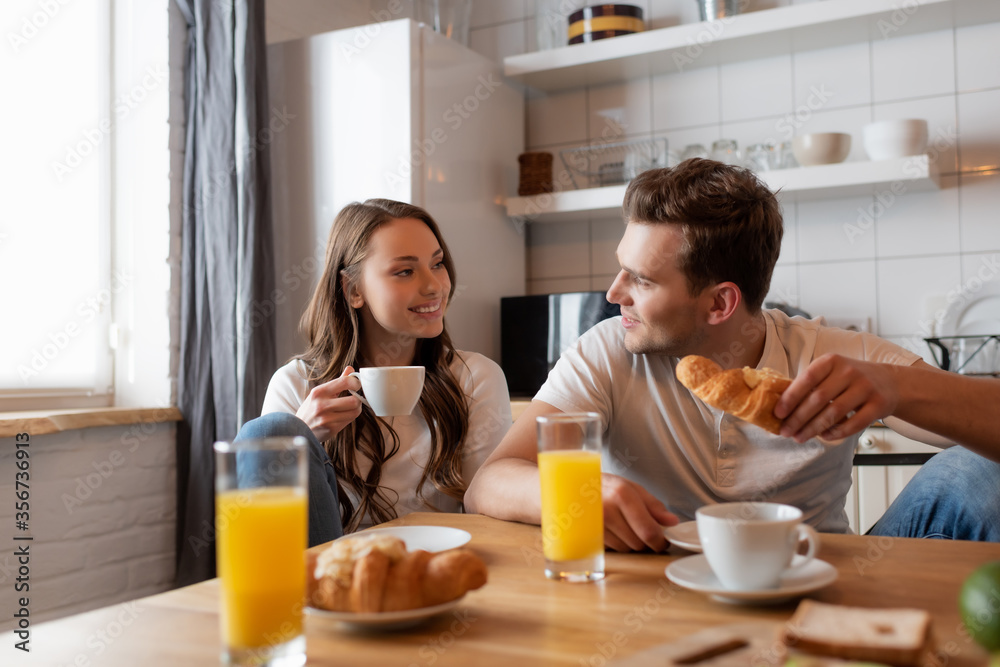 selective focus of cheerful couple looking at each other near delicious breakfast on table