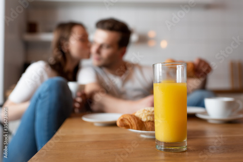 selective focus of glass with fresh orange juice near croissant and couple