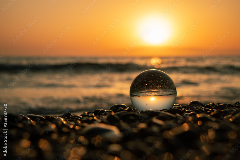 Stones on the ocean shore and waves and splash is reflected in a crystal ball at sunset Stones on the ocean shore and waves and splash is reflected in a crystal ball at sunset