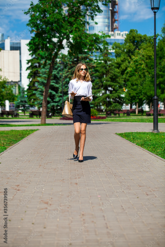 Young business blonde woman walks in a summer park