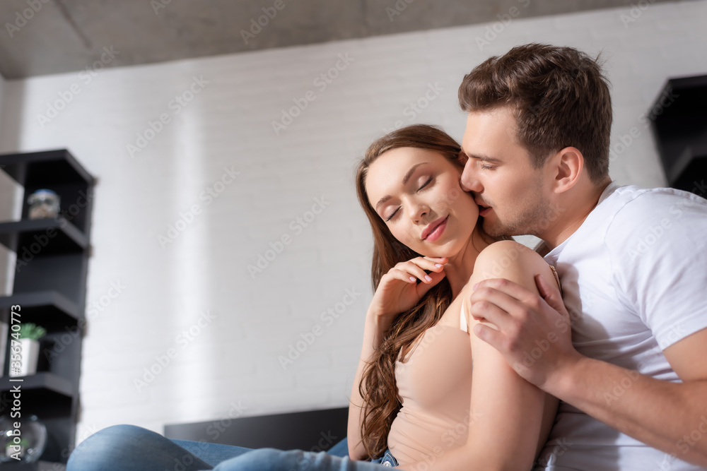 handsome man with closed eyes kissing neck of beautiful and happy girl