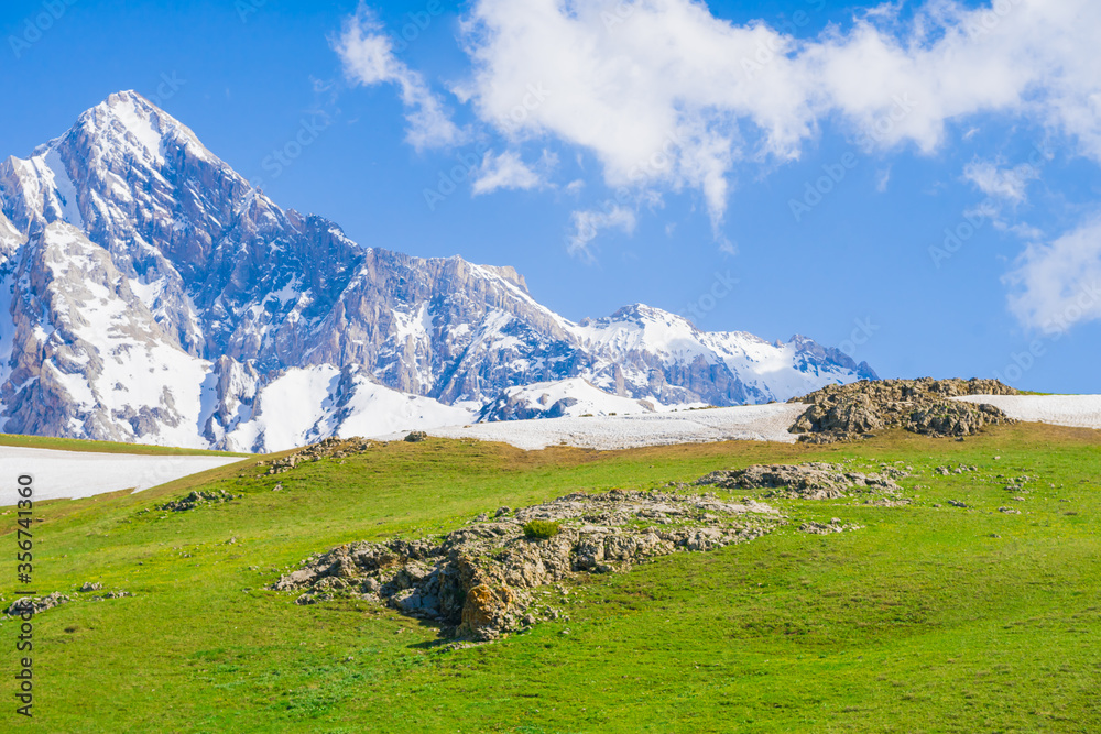 Clouds in the mountains. Spring mountain landscape. Meadow with green grass and flowers. Mountain tourism. The beauty of the Tien Shan mountains. Alpine meadows.