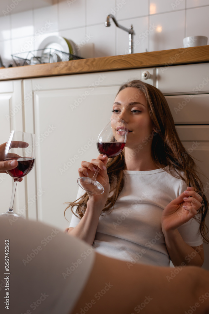 selective focus of woman holding glass with red wine and touching hair while looking at man selective focus of woman holding glass with red wine and touching hair while looking at man