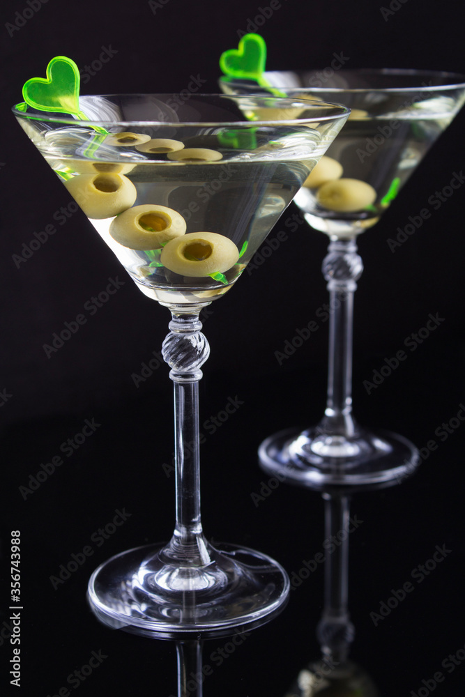 Martini with green olives in two glasses  on a black background, location vertical