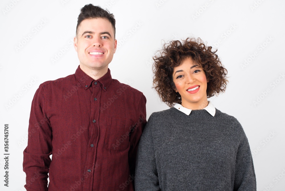 Confidence and business concept. Portrait of charming successful young man and woman, smiling broadly with self-assured expression while holding hands in pockets standing against gray wall. Confidence and business concept. Portrait of charming successful young man and woman, smiling broadly with self-assured expression while holding hands in pockets standing against gray wall.