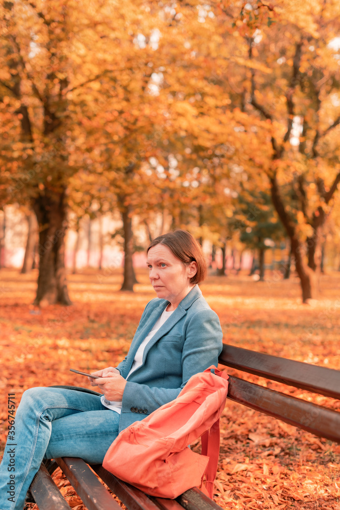 Woman typing text message on mobile phone on park bench Woman typing text message on mobile phone on park bench