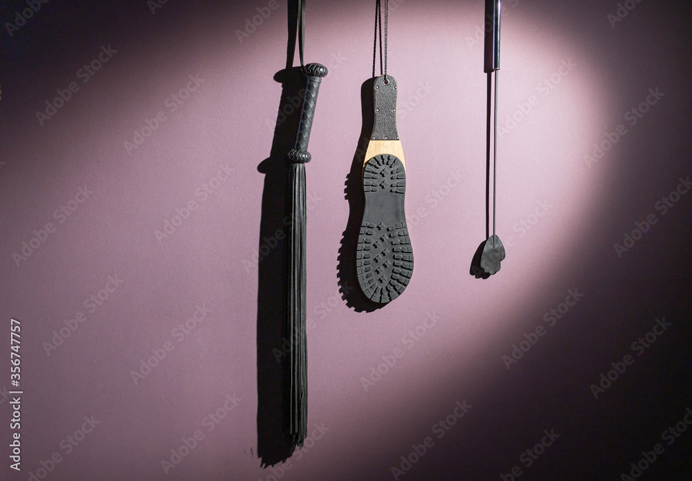 A diverse collection of leather lashes with fringe and a sole for sexual  pleasures are hanging on the wall. Sex equipment for punishment and spanking  for role-playing games. BDSM room. Stock Photo