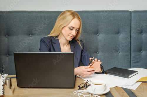 Young woman is using smartphone sitting at wooden table in coffee shop.
