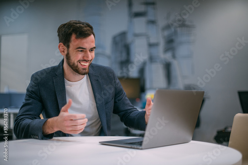 Portrait of contemporary young businessman at a working laptop. Young handsome positive man in a jacket in the interiors of a modern office. photo