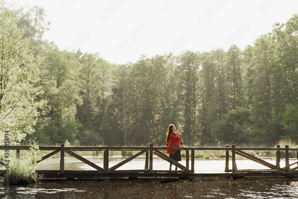 Georgian woman in red national dress with cross symbols. Attractive woman on the lake with forest background. Georgian culture lifestyle. Woman looks right side