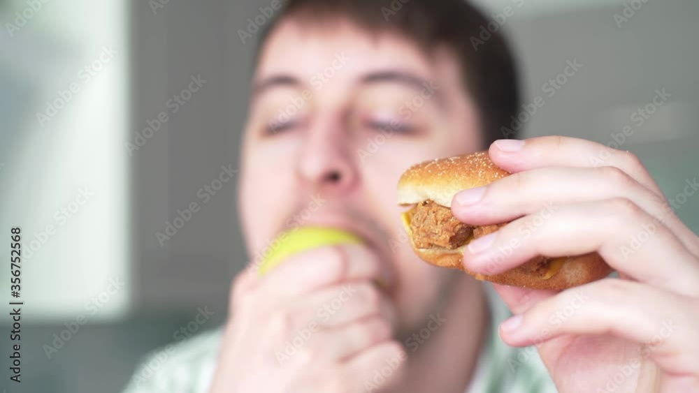 Choosing healthy or unhealthy food. Hungry man bites apple on the background cheeseburger Choosing healthy or unhealthy food. Hungry man bites apple on the background cheeseburger
