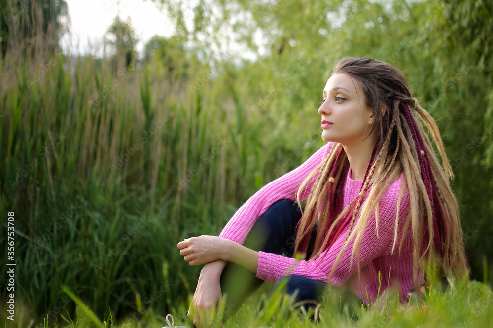 Outdoors female portrait of a girl with dreadlocks wearing pink sweater in a city park during a sunset, be free concept. Outdoors female portrait of a girl with dreadlocks wearing pink sweater in a city park during a sunset, be free concept.