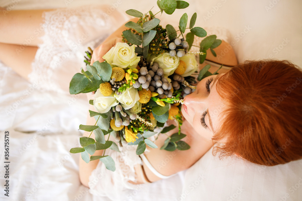 Naklejka premium Pretty bride in a transparent peignoir lies on the bed with a bouquet in her hands. Boudoir morning of the bride. Top view.