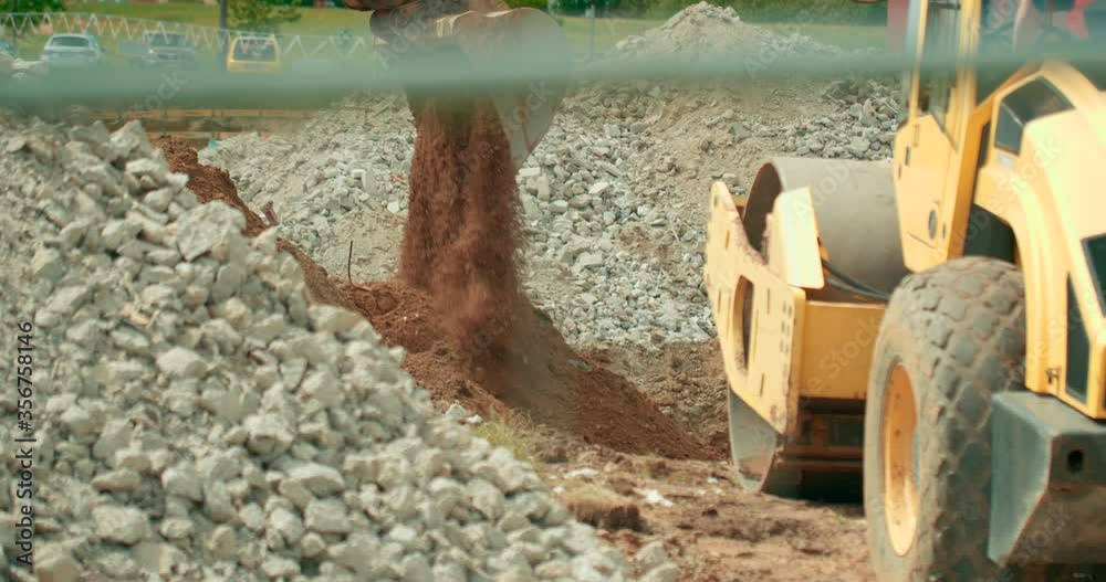 View of construction site excavation moving the soil and a soil compactor working in the site. View of construction site excavation moving the soil and a soil compactor working in the site.