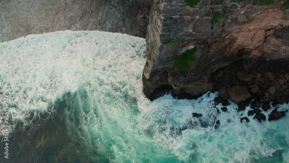 Aerial view of ocean blue waves break on high cliff of a rocky mountain. Danger sea waves on a beach aerial view drone shot. Bird's eye view of ocean waves crashing on a big stones on empty stone. Aerial view of ocean blue waves break on high cliff of a rocky mountain. Danger sea waves on a beach aerial view drone shot. Bird's eye view of ocean waves crashing on a big stones on empty stone.