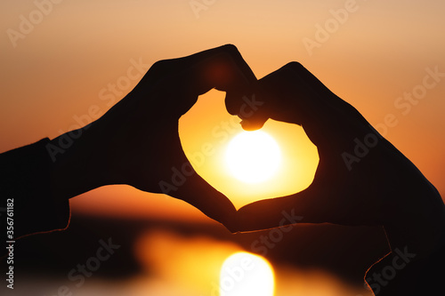silhouette of female hands forms a heart on a sunny sunset sky. love and gratitude. beautiful view on the beach