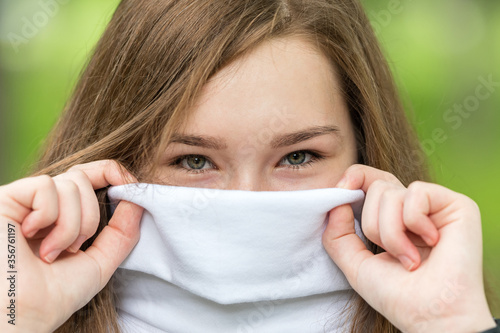 Expressive eyes of a young girl, brunette. The wide collar of her white sweater covers her face. On a green background.