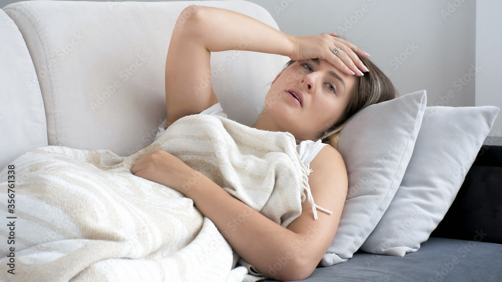 Portrait of woman suffering from migraine lying on sofa under blanket