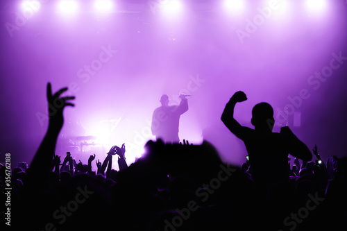 silhouette of musicians on the festival stage in purple light with a dancing crowd of fans in the hall. music concert poster or banner. cool festival atmosphere
