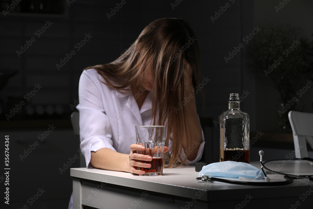 woman drinking alcohol in the kitchen. Young woman suffering from strong headache or migraine sitting with glass of whiskey in the kitchen. alcohol dependence woman drinking alcohol in the kitchen. Young woman suffering from strong headache or migraine sitting with glass of whiskey in the kitchen. alcohol dependence