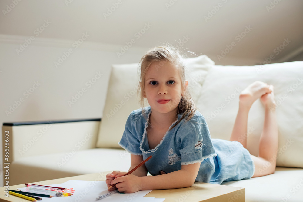 the girl is lying on a white sofa and drawing the girl is lying on a white sofa and drawing